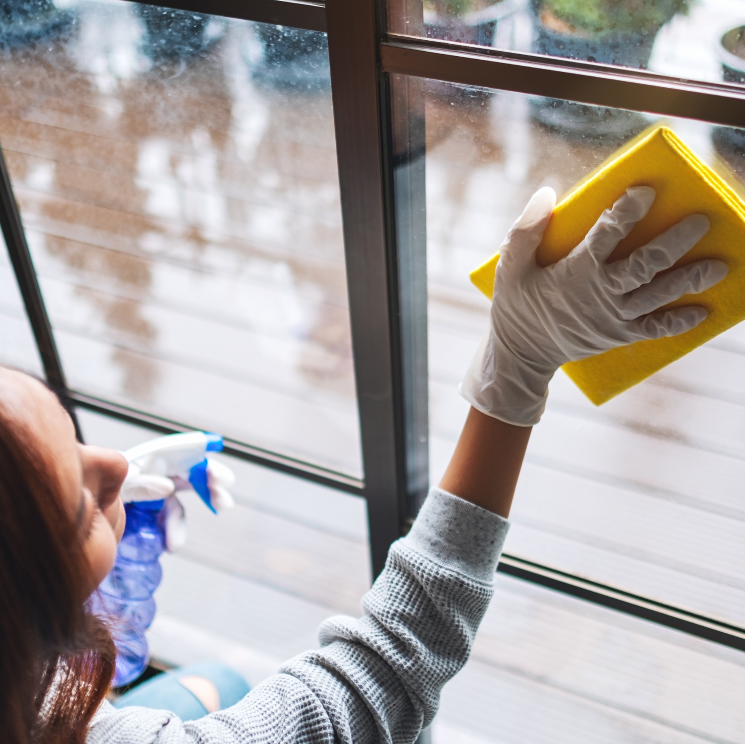 A young woman wearing protective glove cleaning the window for h Nainen pyyhkii ikkunalasia.